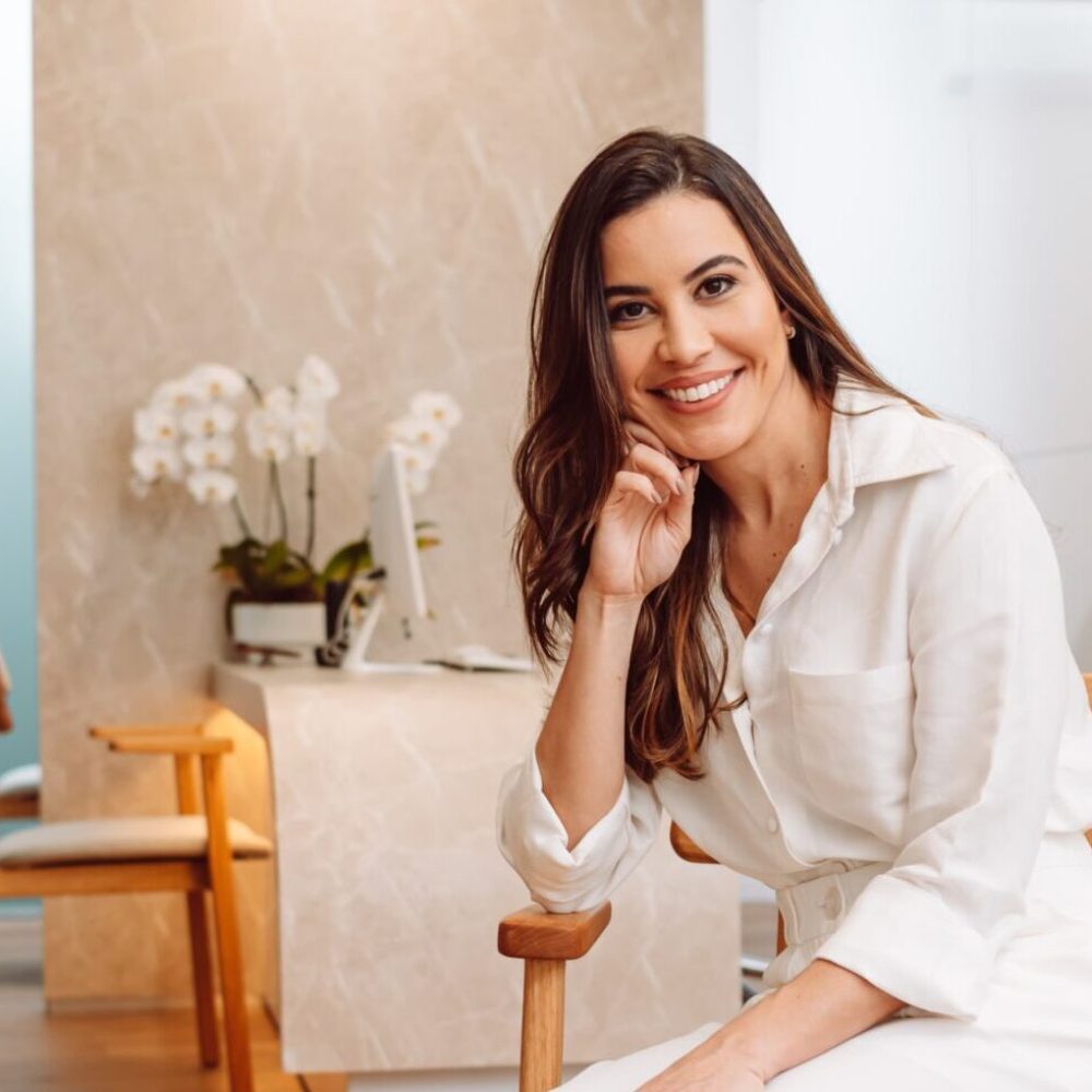 Dra. Laís Carvalho, ginecologista em Belo Horizonte, sentada no hall da Clínica Cavalieri em ambiente moderno e acolhedor.